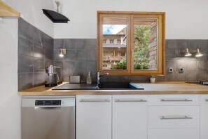 Eine moderne Küche mit Geschirrspüler, Kaffeemaschine und einem Fenster mit Blick auf ein Steinhaus.