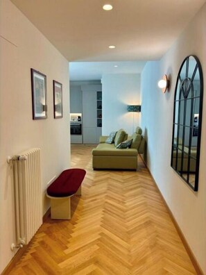 Ein Flur mit Fischgrätparkett, einem Heizkörper, einer Bank, einem Sofa mit Kissen und einem großen Fenster mit Blick.