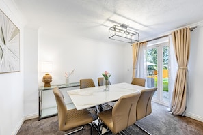A dining area with a table and chairs, a vase with flowers, and a lamp. - Luxury 4 Bedroom Home, Sleeps 10, Garden, Free Parking, Hornchurch, Near London (Hornchurch)
