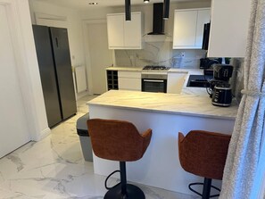 A modern kitchen with a marble countertop, two stools, a coffee maker, and a gas stove. - Luxury 4 Bedroom Home, Sleeps 10, Garden, Free Parking, Hornchurch, Near London (Hornchurch)