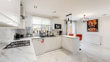 A modern kitchen with white cabinetry, a gas stove, a microwave, and a sink.