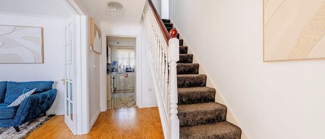 Una escalera con barandilla de madera y peldaños alfombrados que conducen a una zona de cocina.