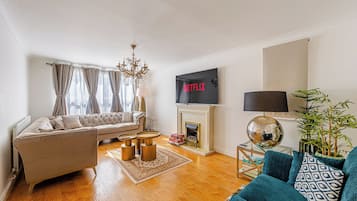 A living room with a sofa, a coffee table, a fireplace, a TV mounted on the wall, and a lamp.