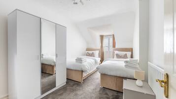 A bedroom with two beds, a wardrobe, a radiator, and a ceiling fan.