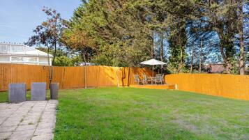 A fenced backyard with a grassy area, a patio with chairs and a table, and a wooden fence.
