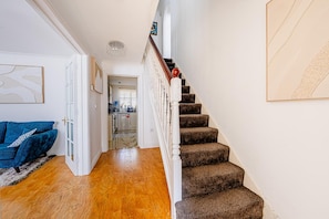A staircase leading to a second floor, a blue sofa, and a kitchen area. - Luxury 4 Bedroom Home, Sleeps 10, Garden, Free Parking, Hornchurch, Near London (Hornchurch)