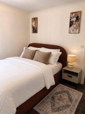 A neatly made bed with white linens and two pillows, a bedside table with a lamp, and a patterned rug on the floor. - Luxury 4 Bedroom Home, Sleeps 10, Garden, Free Parking, Hornchurch, Near London (Hornchurch)