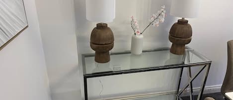 Una mesa de centro con superficie de vidrio, dos lámparas de madera y un jarrón con flores.