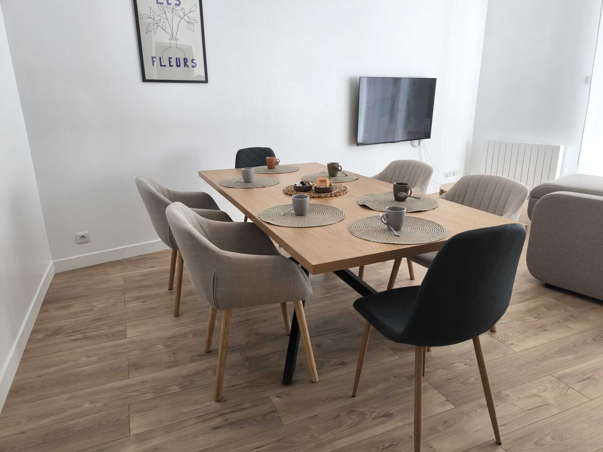 A dining area with a wooden table, six chairs, and a TV mounted on the wall.