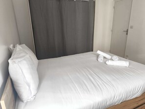 Ein Einzelbett mit weißer Bettwäsche, einem grauen Vorhang und einem hölzernen Kopfteil.