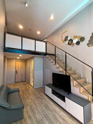 A modern living room with a TV, sofa, and staircase.