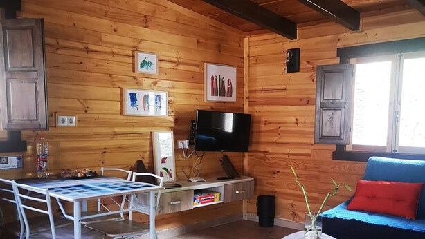 Ein Holzinnenraum mit einem Esstisch, Stühlen, einer Couch, einem Fernseher und gerahmten Bildern an der Wand.