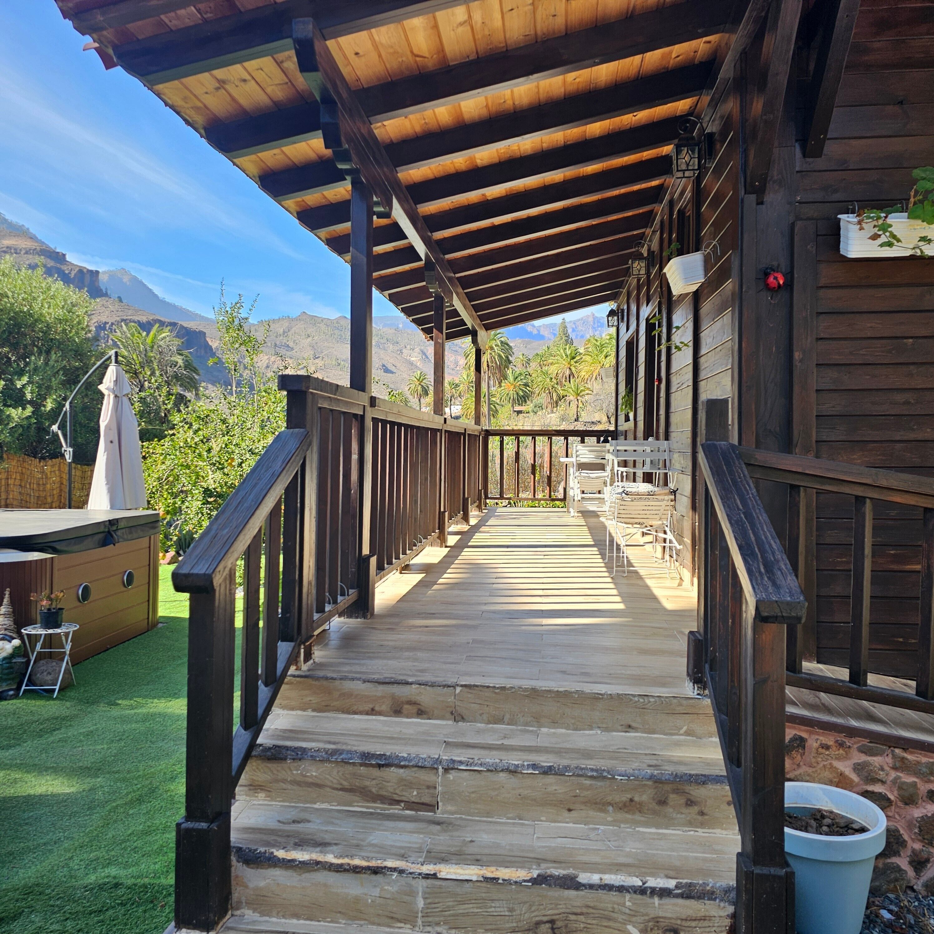Eine Holzterrasse mit Geländer, die zu einem überdachten Veranda-Bereich führt, mit Blick auf eine gebirgige Landschaft.