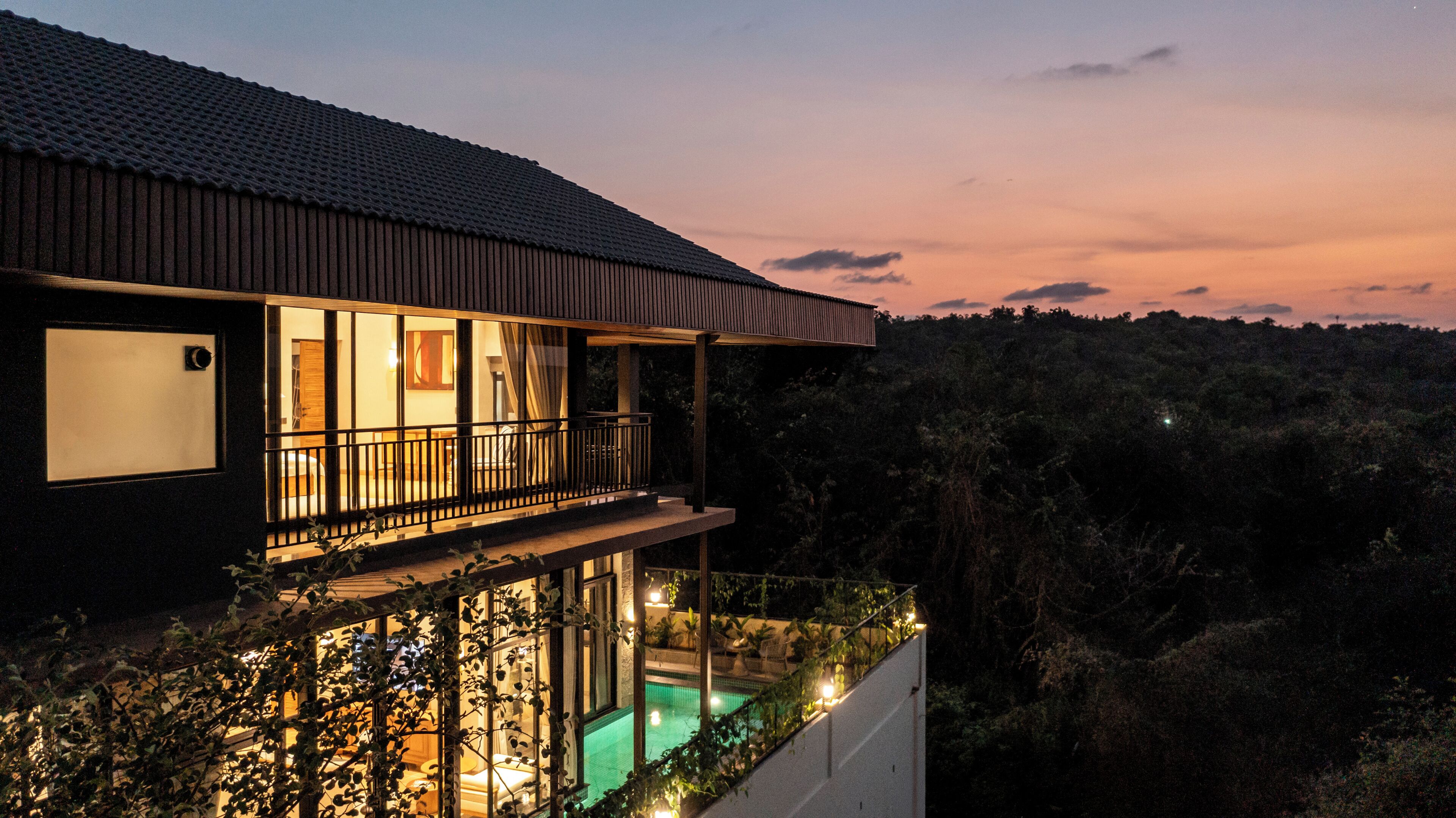 A modern house with a balcony overlooking a swimming pool, surrounded by dense vegetation.