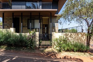A modern two-story building with a balcony, a gated entrance, and a variety of plants in the foreground. - Staymaster Timber Ridge - 4BR with Pool (Sangolda)
