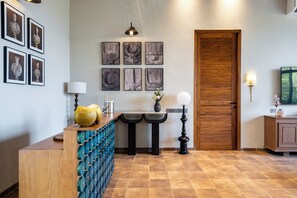 Un vestíbulo de hotel con mostrador de recepción, obras de arte enmarcadas, una puerta de madera y suelo de baldosas.