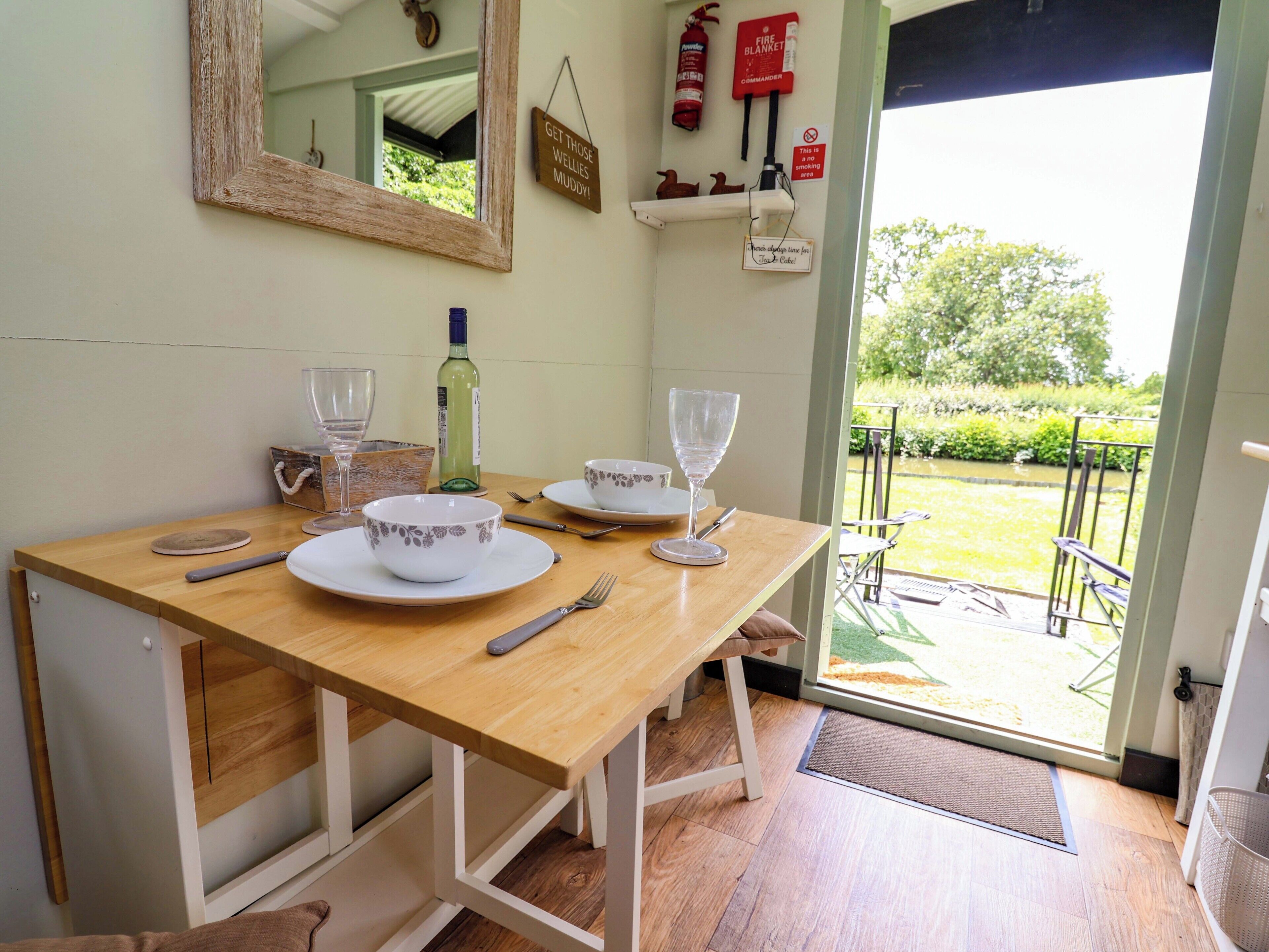 A dining table with plates, glasses, and cutlery, a bottle of wine, a mirror, and a fire extinguisher.