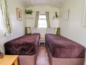 A room with two beds, a small table, and a window with curtains. - Hop To It (Whitchurch)