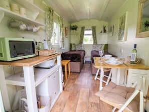 A compact room with a kitchenette, a dining area, and a seating area with a sofa and a chair. - Hop To It (Whitchurch)