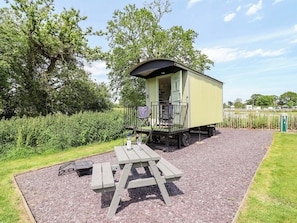 A small, single-story structure with a covered porch, a picnic table, and a gravel area. - Hop To It (Whitchurch)