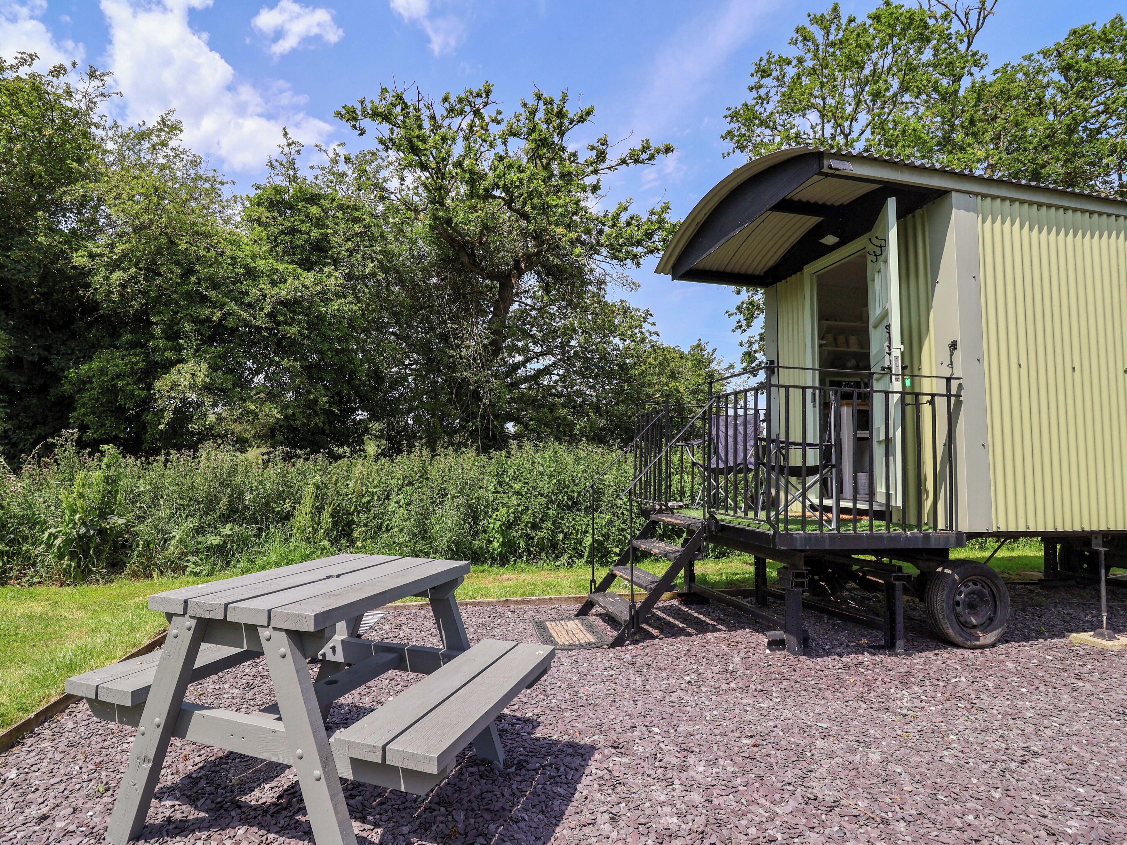 A rustic wooden picnic table and a small green building with a balcony, surrounded by lush greenery.