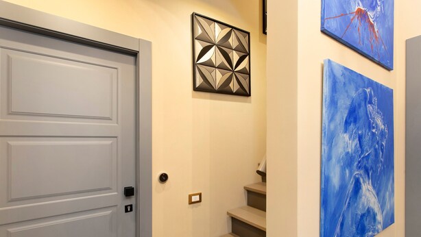 Eine Treppe mit einer Tür links, einem geometrischen Wandbild darüber und zwei abstrakten Gemälden rechts an der Wand.