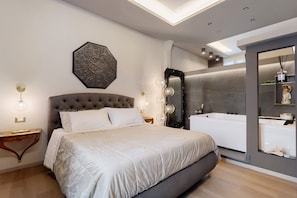 A modern bedroom with a large bed, a decorative wall piece, a vanity with a mirror, and a bathtub. - Archs - Queen Apartment with Balcony, Wi-Fi, and Air Conditioning (Catania)