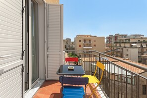 A balcony with a table and chairs, a sliding door, and a view of surrounding buildings. - Archs Apartment - Deluxe in Catania (Catania)