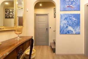 Un couloir avec un banc en bois, une table en verre, un bol décoratif, une porte et deux œuvres d’art encadrées accrochées au mur.