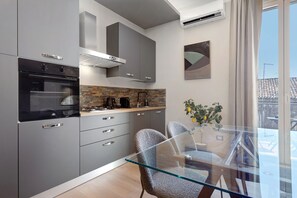 A modern kitchen with grey cabinets, a built-in oven, and a gas stove. There is a glass table with two chairs and a vase with flowers. - Archs Apartment - Deluxe in Catania (Catania)