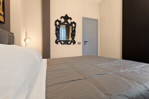 A hotel room with a large bed, a wall-mounted mirror, a door, and a light fixture. - Archs Apartment - Deluxe in Catania (Catania)