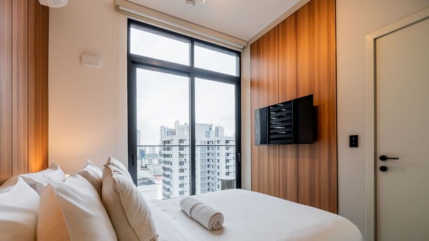 A hotel room with a large window, a bed with white linens, a flat-screen TV mounted on the wall, and a wooden panel wall. - w Deluxe 2BR w Balcony View in San Francisco (Panama City)