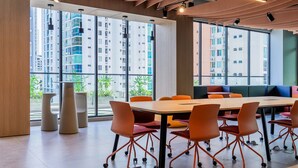 A modern conference room with a large table and orange chairs, large windows with a view of high-rise buildings, and a wooden ceiling with track lighting. - w Deluxe 2BR w Balcony View in San Francisco (Panama City)