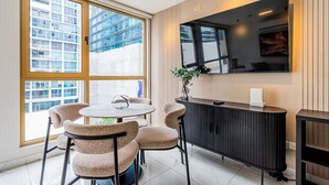 Ein modernes Zimmer mit einem runden Tisch, vier Stühlen, einem Schrank und einem großen Fenster mit Blick auf Gebäude.