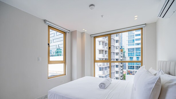 Ein modernes Hotelzimmer mit einem großen Bett, zwei Fenstern mit Holzrahmen und Blick auf die Stadt.
