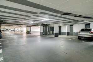 A multi-level parking garage with concrete floors and walls, multiple parking spaces, and a few cars parked. - Safe 2 Bed With View in The Waterclub Bella Marina (Cape Town)