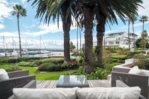 A patio with wicker furniture, a glass-top table, and a view of a marina with boats. - Safe 2 Bed With View in The Waterclub Bella Marina (Cape Town)