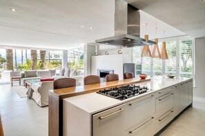 A modern kitchen with a central island, stainless steel appliances, and a dining area with a sofa and chairs. - Safe 2 Bed With View in The Waterclub Bella Marina (Cape Town)