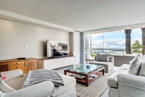 A modern living room with a TV, sofa, and a glass coffee table. - Safe 2 Bed With View in The Waterclub Bella Marina (Cape Town)