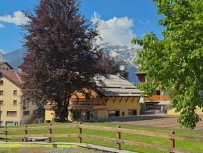 A building with a sloped roof, a wooden fence, and a mountain in the background. - The Clotes Hideaway - Steps From Chairlift (Sauze d'Oulx)