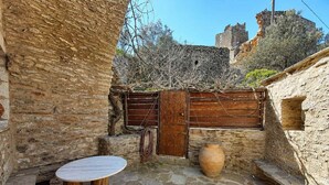 A stone courtyard with a round table and a wooden bench, a rustic wooden gate, and a large clay pot. - Vathia Tower - Stone Mani Heaven Near the Beach (East Mani)