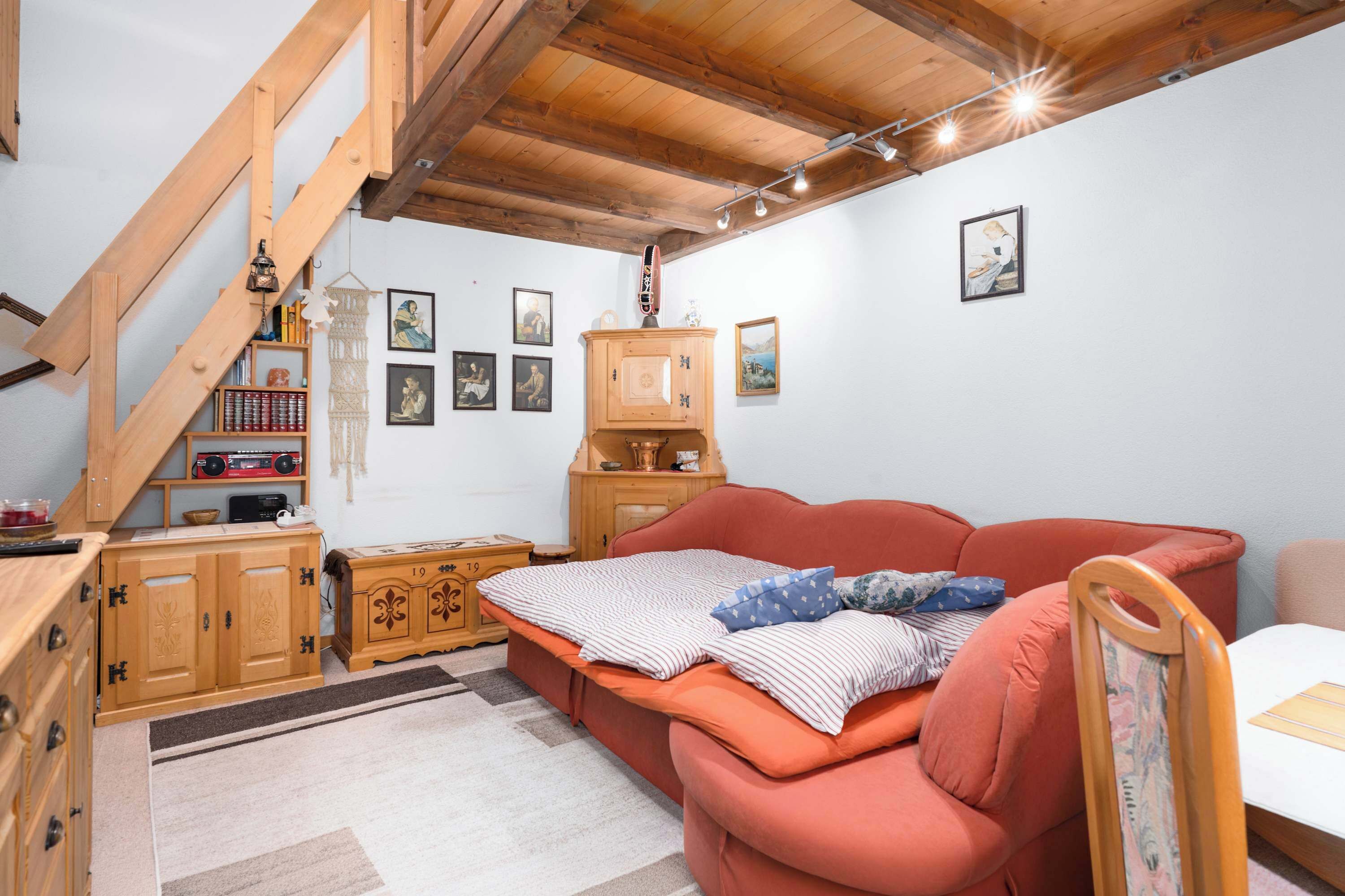 A cozy room with a wooden staircase, a red sofa, and a wooden cabinet.