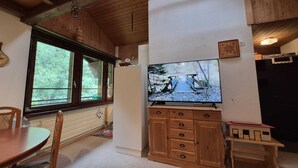 Una habitación con techo de madera, un televisor montado en una pared blanca, un mueble de madera y una mesa de comedor con sillas.