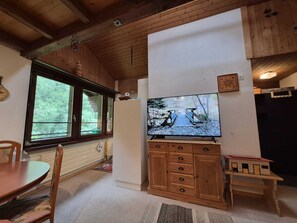 Una habitación con techo de madera, un televisor montado en una pared blanca, un mueble de madera y una mesa de comedor con sillas.