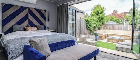 A bedroom with a large bed, a sofa, a sliding glass door to a patio, and a view of the outside.