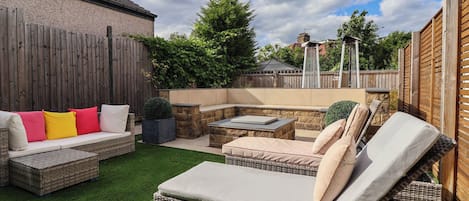 A backyard with a wicker sofa, a dining table, and a barbecue area.