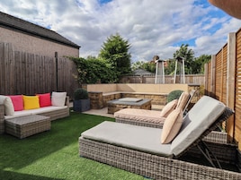 A backyard with a wicker sofa, a dining table, and a barbecue area.