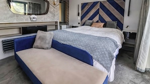 A modern hotel room with a large bed, a sofa, a TV, and a wall-mounted air conditioner. - The Annexe (Shipley)