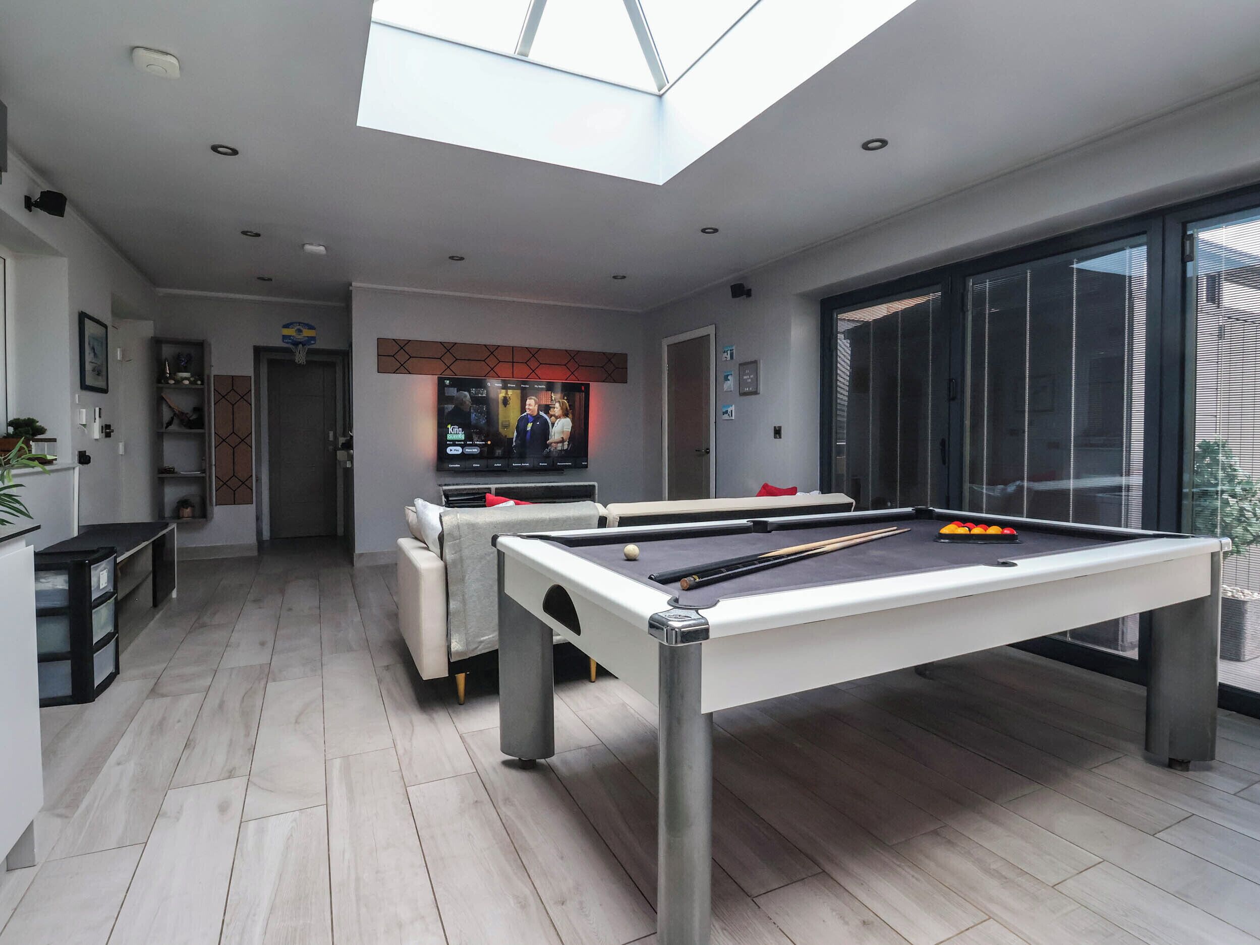 A modern living room with a pool table, a television, and a skylight.