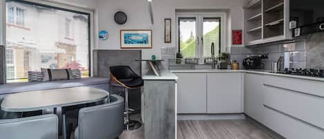 A modern kitchen with a dining area, featuring a central island, grey cabinetry, and a view of the outdoors.